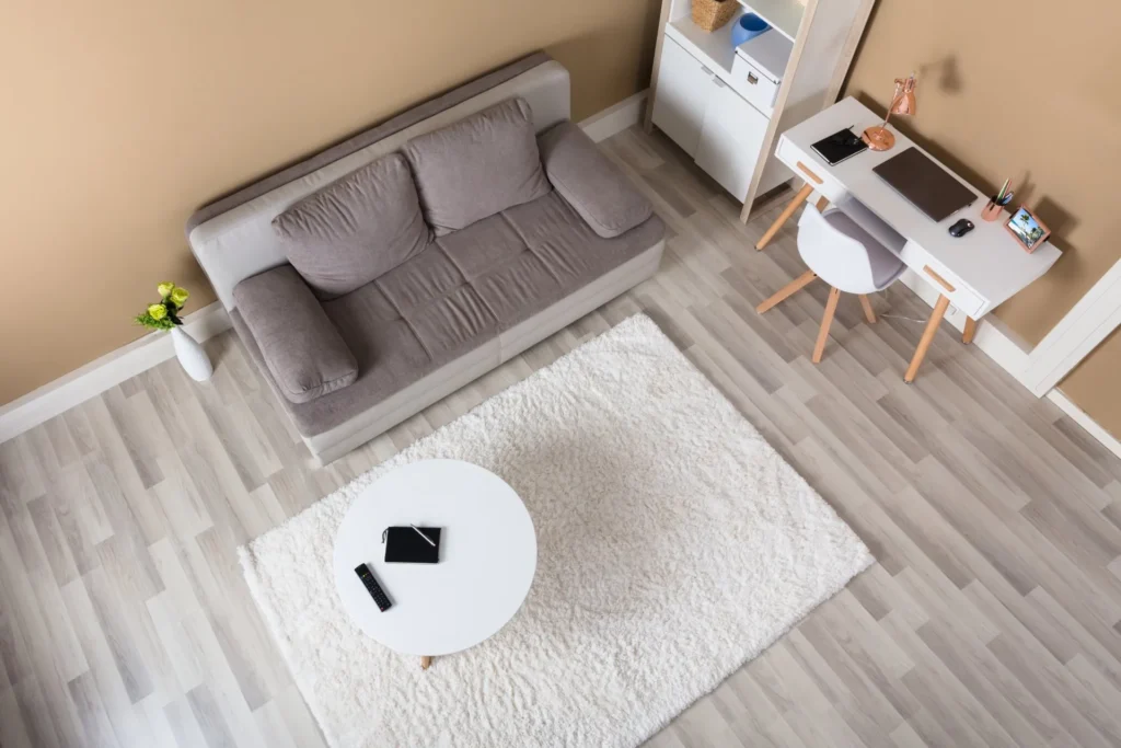 Overhead view of a living room with grey sofa, white rug and pale wood floor